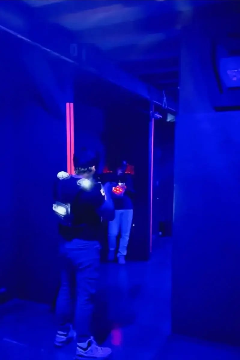 Zwei Personen in dunklem Raum mit blauer Neonbeleuchtung spielen Lasertag. Leuchtende Westen und Lichteffekte sorgen für eine futuristische Atmosphäre. Symbolisiert Freizeitaktivität, Teamspiel oder Adrenalin-geladenen Wettbewerb.